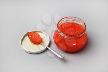 Fresh delicious red caviar. Red caviar in glass jar and spoon on gray background.
