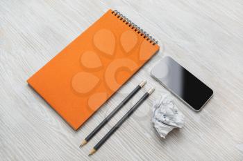 Blank business stationery set on light wooden background. Smartphone, blank orange notepad, pencils and crumpled paper.