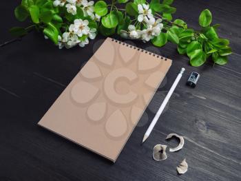 Photo of closed blank kraft notebook, pencil, sharpener and spring flowers on wooden background. Template for placing your design.