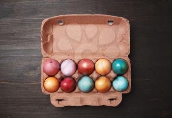 Packaging with colored Easter eggs on wood table background. Flat lay.