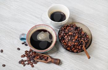 Delicious fresh coffee. Coffee cups and coffee beans on light wooden background.