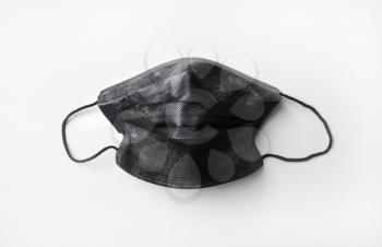 Black medical protective face mask on white table background. Flat lay.