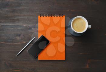 Orange notebook, smartphone, coffee cup and pen on wood table background. Blank branding template. Flat lay.