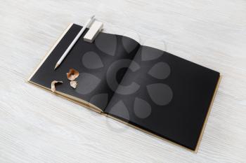 Blank black book, pencil and eraser on light wood table background. Stationery template.