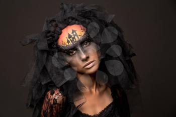 Halloween devil's bride. Portrait of young woman in dark artistic image with scary makeup, veil and terrible picture on her forehead.