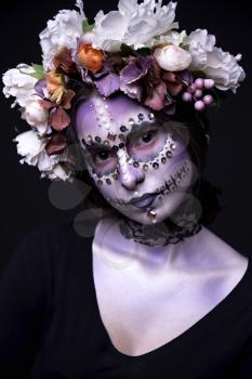 Fashion portrait of a beautiful Halloween model with creative make up,  rhinestones and wreath of flowers on black background