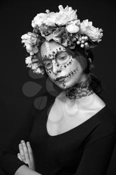 Artistic black and white portrait of a beautiful Halloween model with creative make up,  rhinestones and wreath of flowers on black background