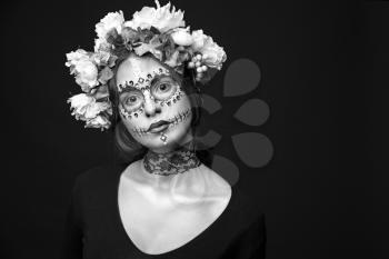 Fashion black and white portrait of a beautiful Halloween model with creative make up,  rhinestones and wreath of flowers on black background