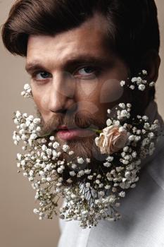Creative Portrait of young beautiful man with a beard decorated with flowers.