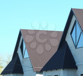 A house with a roof made of metal sheets. The house with gables, windows and metal roof, equipped with overflow and protection from snow.