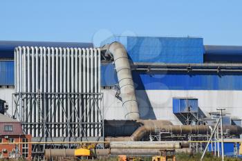 Big plant for processing scrap metal. Huge factory old metal refiner. Blue roof of the factory building. Exhaust pipes, radiators, cooling industrial units as well as office buildings.