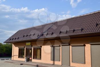 The roof of corrugated sheet on a building. Brown roofing metal sheets on Rented store. Brown shutters on the windows.