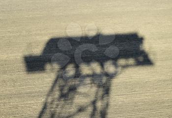 The shadow of a water tower on a plowed field.