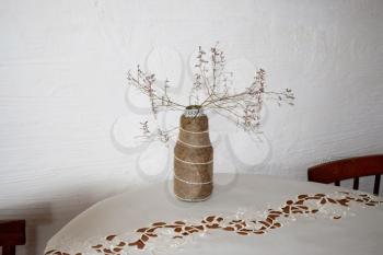 Vase from a bottle wrapped in rope. Dry twigs in a vase on the table.