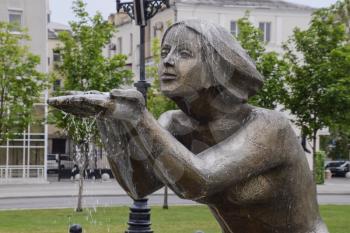 Statue of kneeling woman in the fountain. Water flowing from the hands of the statue.