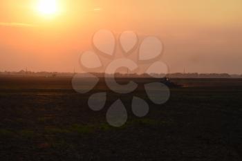 Tractor plowing plow the field on a background sunset. tractor silhouette on sunset background.