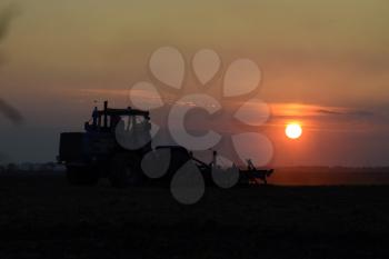 Tractor plowing plow the field on a background sunset. tractor silhouette on sunset background.