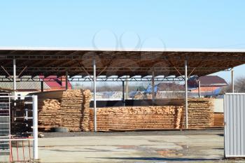 Warehouse of building materials, wood planks stacked under a canopy.