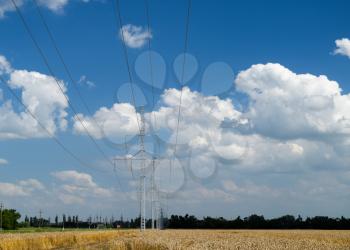 A transmission line on a background of wheat fields and sky with clouds.