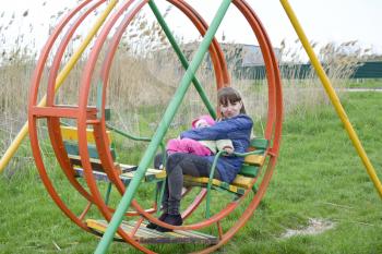 A young mother with her baby on the playground. Young mother on a swing