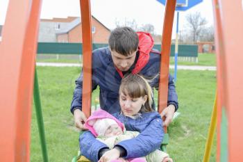 Young married couple with child in playground. Young family on a swing.