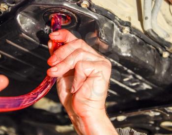 Oil change in automatic transmission. Filling the oil through the hose. Car maintenance station. Red gear oil. The hands of the car mechanic in oil.