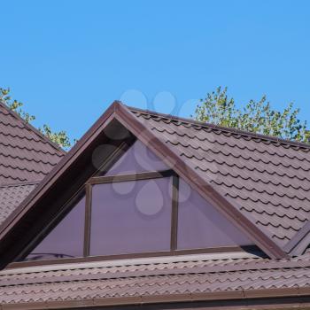 House with plastic windows and a brown roof of corrugated sheet. Roofing of metal profile wavy shape on the house with plastic windows.