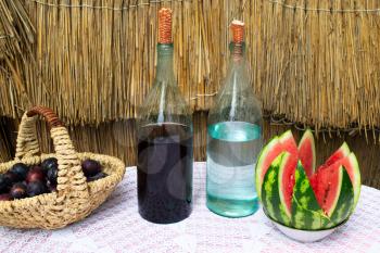 Bottles of wine and moonshine on the table. A basket with a plum and a watermelon as a snack. Traditional alcoholic drinks.