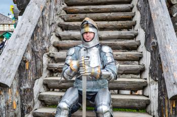 Knight in the armor on the wooden steps. Knightly armor and weapon. Semi - antique photo.