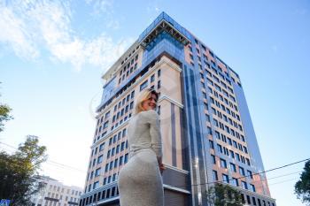 A girl with a beautiful figure in a gray dress near a tall building