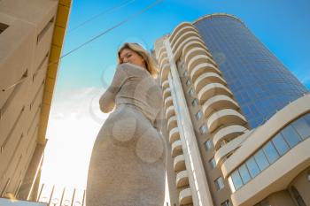 A girl with a beautiful figure in a gray dress near a tall building