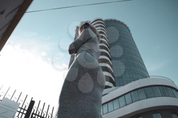 A girl with a beautiful figure in a gray dress near a tall building