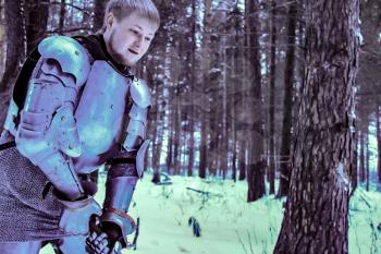 Knight in armor and with a sword in the middle of a winter forest. Vintage military uniform.