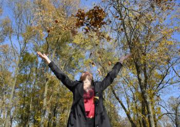 A woman throws up the autumn yellow leaves. Autumn in the park.