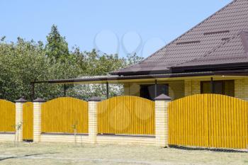 Brick house with corrugated metal profile roof and wooden fence. Beautiful view of the facade. Style of design.