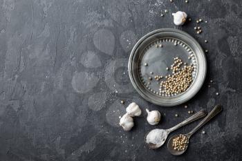 White pepper, garlic and salt on dark grey culinary background, various spices, directly above, flat lay, copy space