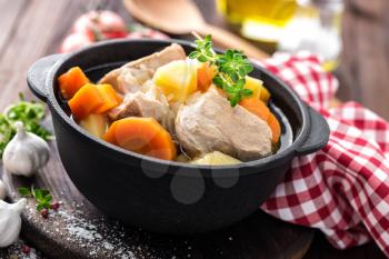 Meat stewed with carrots and potatoes in sauce on wooden rustic background