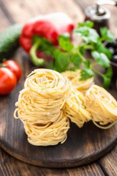Raw all'uovo pasta, egg noodles with cooking ingredients on dark wooden rustic background, traditional italian cuisine