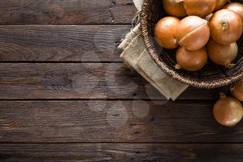 Fresh onion in basket on wooden table, top view