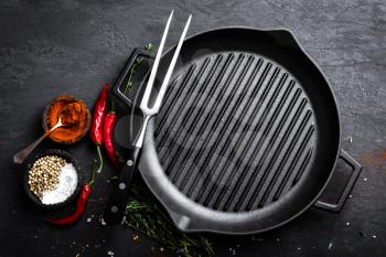 Empty cast-iron grill pan with ingredients for cooking on black background, top view