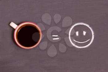 A cup of coffee and smiling smiley drawn with chalk on the table. The concept of a good morning. Energy from coffee.