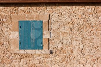 Antique wall of stone and blue wooden shutters on the window. Traditional vintage walnut, cypriot european style