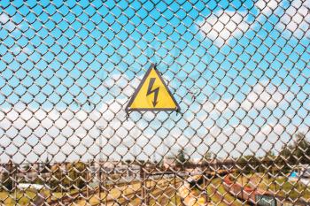 Yellow sign of danger on the fence, the grid