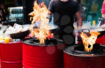 Cooking food in pans at a street festival, fire with red barrels.