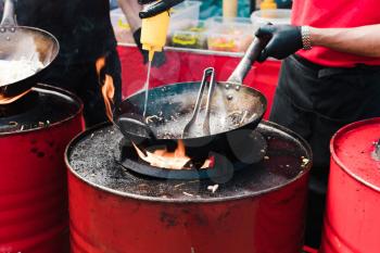 Cooking food in pans at a street festival, fire with red barrels.