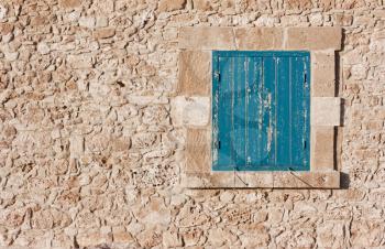 Antique wall of stone and blue wooden shutters on the window. Traditional vintage walnut, cypriot european style