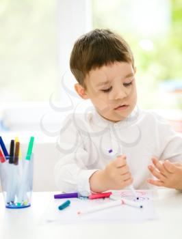 Little boy is drawing on white paper using color pencils