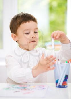 Little boy is drawing on white paper using color pencils