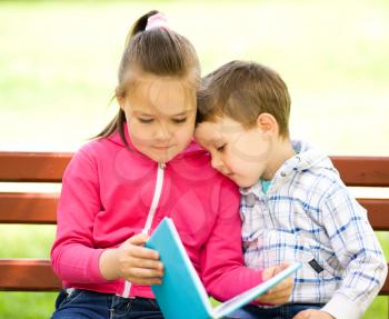 Little boy and girl is reading book while sitting on green grass outdoors