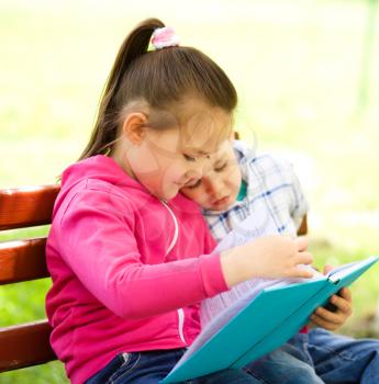 Little boy and girl is reading book while sitting on green grass outdoors
